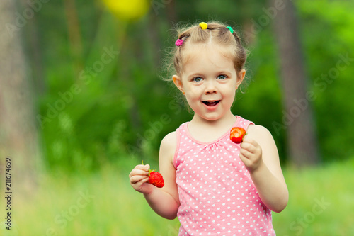 Little girl eating strawberry in nature. Child enjoys a delicious berry.