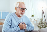 Heart disease symptoms. Attentive senior man touching chest and wearing glasses