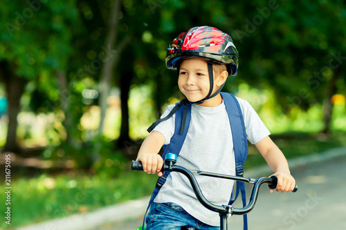 Little boy learns to ride a bike in the park near the home. Portrait of a cute kid on bicycle. Happy smiling child in helmet riding a cycling.