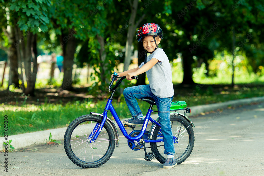 Little boy learns to ride a bike in the park near the home. Portrait of a cute kid on bicycle. Happy smiling child in helmet riding a cycling. Little boy learns to ride a bike in the park near the home. Portrait of a cute kid on bicycle. Happy smiling child in helmet riding a cycling.
