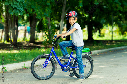 Little boy learns to ride a bike in the park near the home. Portrait of a cute kid on bicycle. Happy smiling child in helmet riding a cycling.