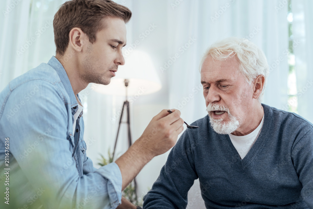 Just eat. Calm man using spoon while senior man opening mouth Just eat. Calm man using spoon while senior man opening mouth