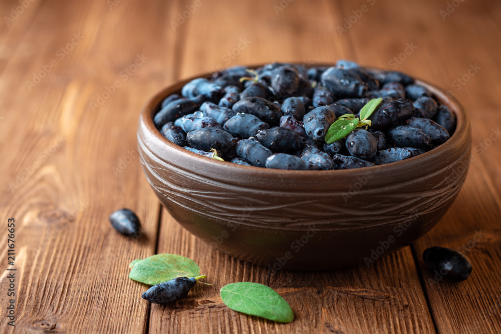 Honeysuckle berries or Lonicera caerulea in ceramic bowl on wooden background Honeysuckle berries or Lonicera caerulea in ceramic bowl on wooden background