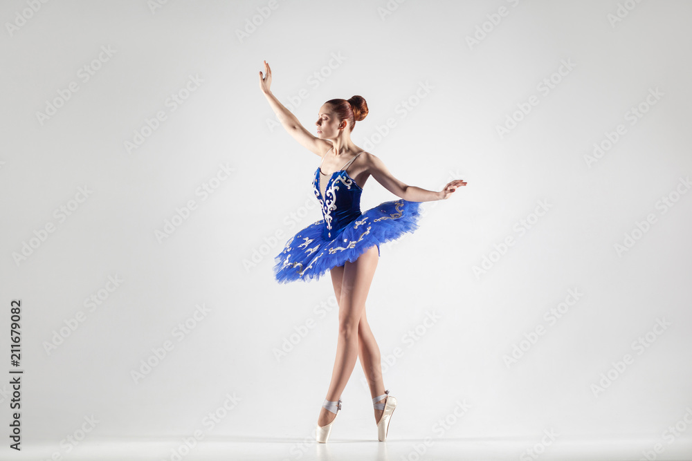 attractive ballerina with bun collected hair wearing blue dress and pointe shoes performing in white studio. attractive ballerina with bun collected hair wearing blue dress and pointe shoes performing in white studio.