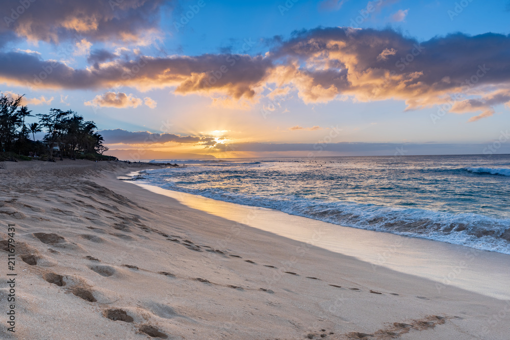 Sunset over Sunset Beach on the North Shore of Oahu, Hawaii with palm trees and surf rolling in on the sandy beach