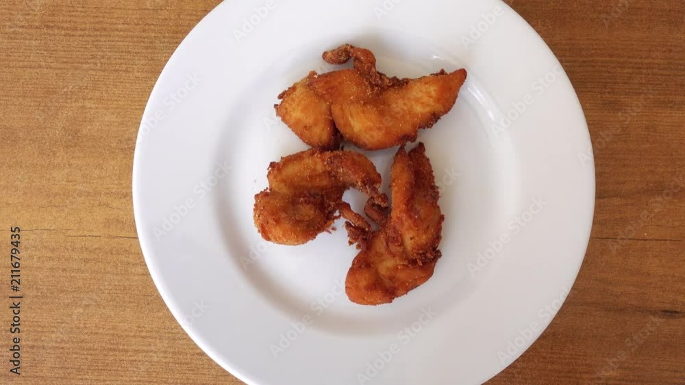 Pieces of meat appetizing chicken in breaded. The chicken on a plate turns on the background of a wooden table. Pieces of meat appetizing chicken in breaded. The chicken on a plate turns on the background of a wooden table.