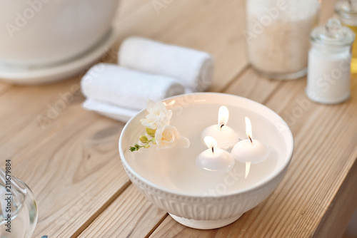 spa set with candles in aroma bath and rolled towels on wooden table.