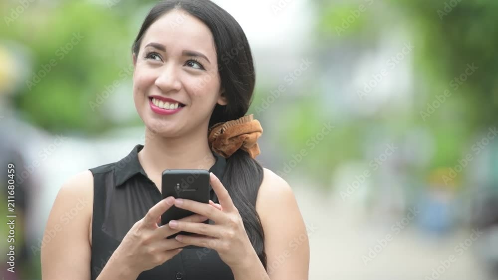 Young beautiful Asian businesswoman using phone in the streets outdoors Young beautiful Asian businesswoman using phone in the streets outdoors