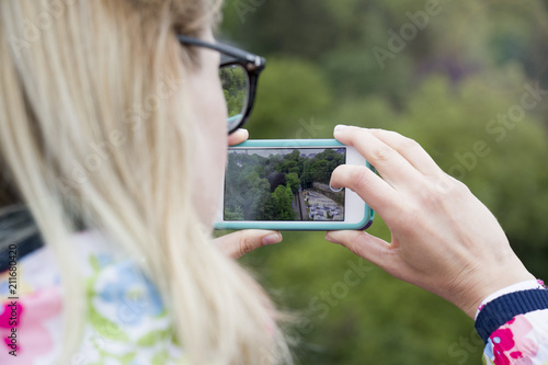 A girl holding a phone to photograph a landscape view.