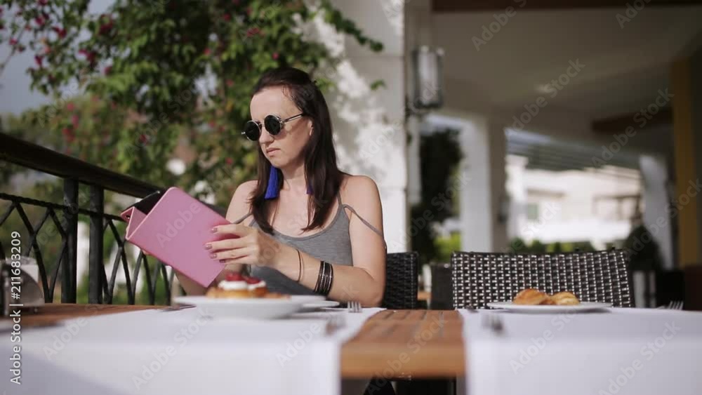 Girl having a breakfast in the bistro and browsing internet on tablet in a street restaurant Girl having a breakfast in the bistro and browsing internet on tablet in a street restaurant