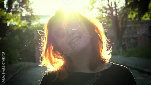 Happy young woman wearing sunglasses tilting her head to side. Portrait of cheerful lady smiling and turning her heaad to side outdoors. photo