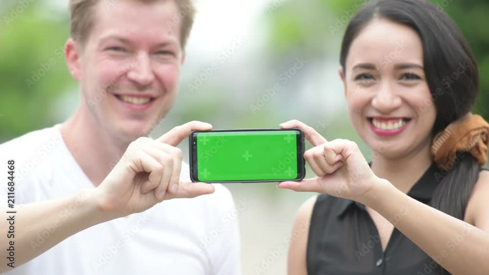 Young multi-ethnic couple showing phone together in the streets outdoors Young multi-ethnic couple showing phone together in the streets outdoors