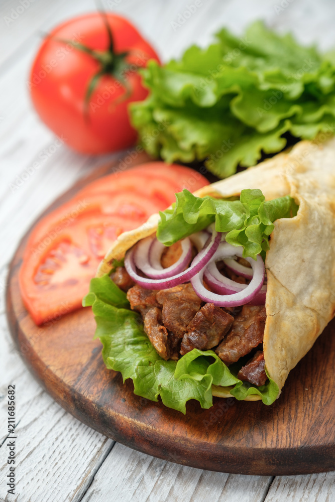 Doner kebab is lying on the cutting board. Shawarma with meat, onions, salad lies on a white old wooden table.