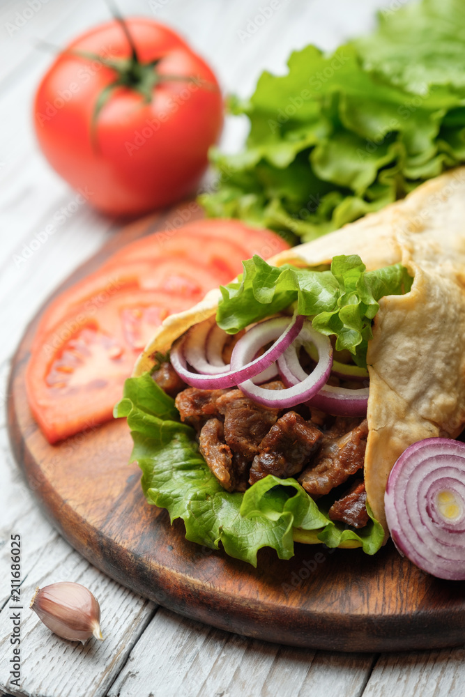 Doner kebab is lying on the cutting board. Shawarma with meat, onions, salad lies on a white old wooden table.