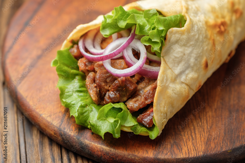 Doner kebab is lying on the cutting board. Shawarma with meat, onions, salad lies on a dark old wooden table. Doner kebab is lying on the cutting board. Shawarma with meat, onions, salad lies on a dark old wooden table.