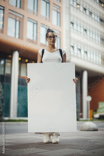 Young Intelligent Attractive Woman Holding Blank Canvas Placard Outdoors. Activist Protesting Against Political and Social Issues. Copy Space. Empty Space. Single Person Protest In The City photo