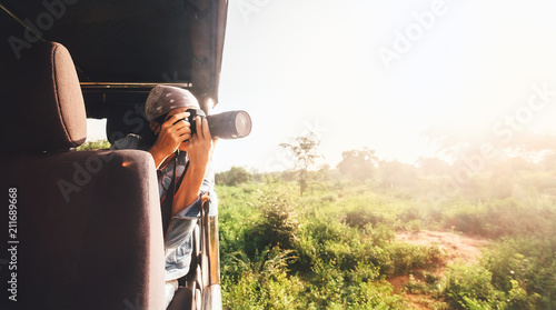 Woman photographer takes a picture with professional camera from touristic vehicle on tropical safari photo