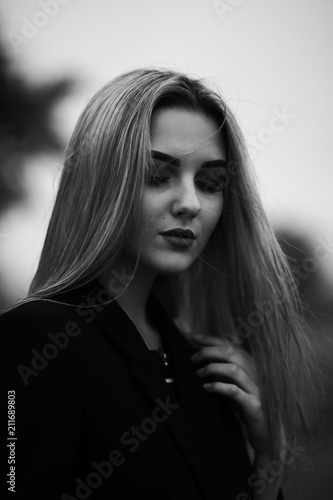 Portrait photos of a girl in a black coat.Girl posing in cloudy weather.Black and white photos of a beautiful blonde