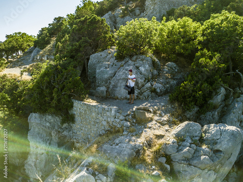 man in casual shirt and shorts with bag standing on the mountain edge and hiking to the top photo