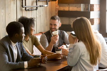 Smiling multiracial people enjoying coffee, talking spending pleasant time together in cozy coffee shop, diverse friends drinking from paper cups, meeting at work break for casual conversation in cafe