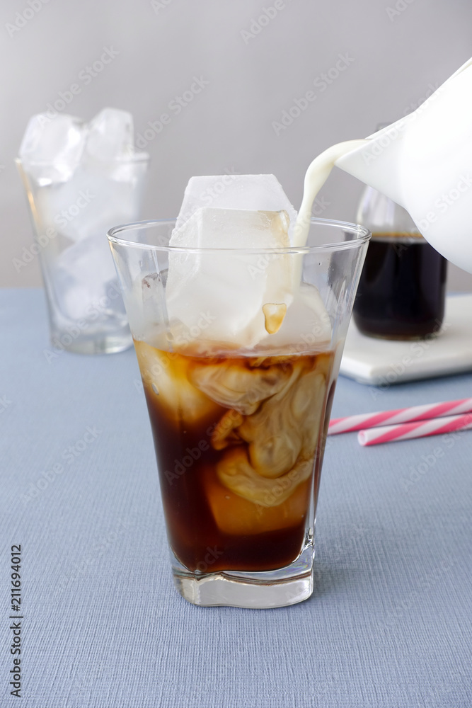 Milk being poured into a glass with cold brew coffee Milk being poured into a glass with cold brew coffee