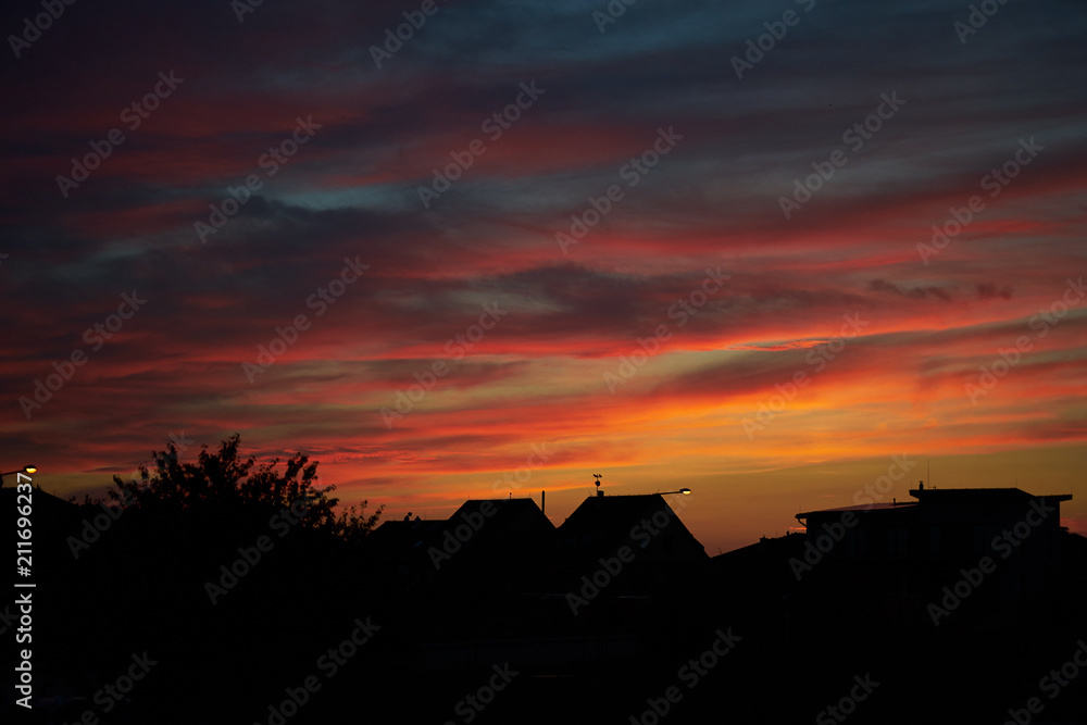 Abstract dynamic composition of the red sky clouds in the sunset above the black silhouette or skyline of the village in Czech republic.