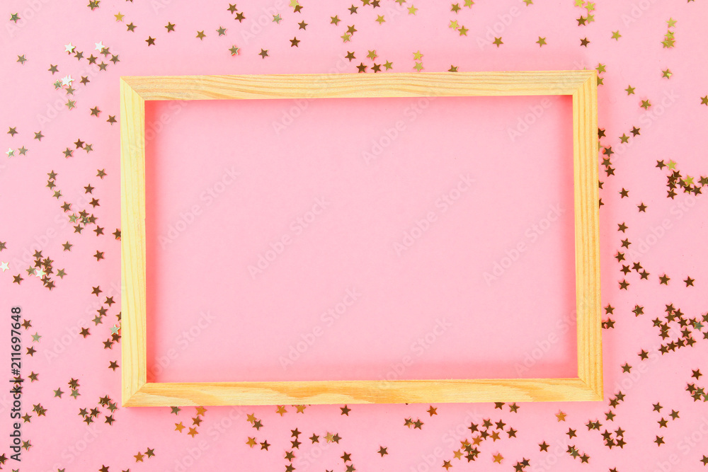 A wooden empty frame on a pastel background surrounded by shiny decorative stars and balls. A wooden empty frame on a pastel background surrounded by shiny decorative stars and balls.