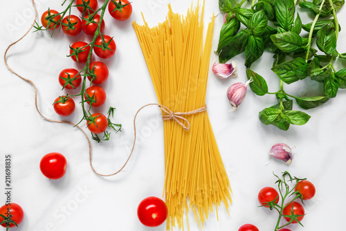Pasta spaghetti with tomatoes, garlic and basil on white marble background. Ingredients for traditional italian dish