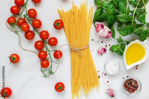 Pasta spaghetti with tomatoes, garlic, olive oil and basil on white marble background. Ingredients for italian dish