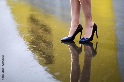 Female feet in shoes on wet asphalt in the rain