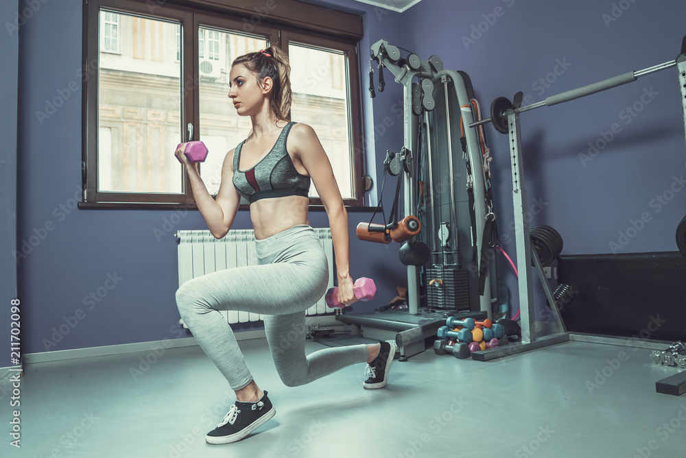 Fototapeta premium Young woman doing exercise at gym, lifting dumbbell weights, kee