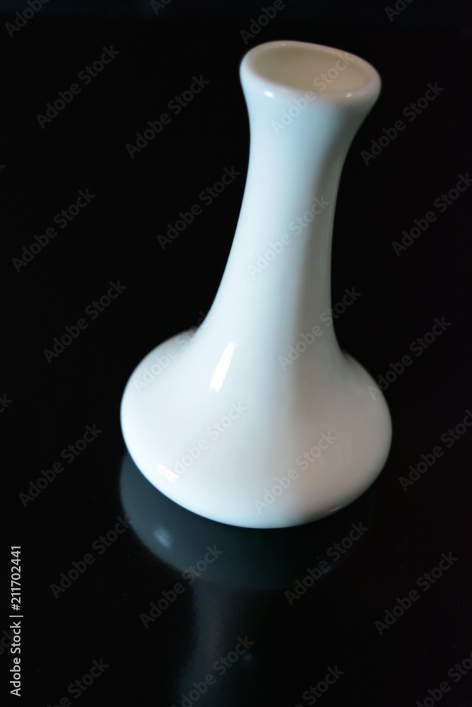 On a black glossy background is a white ceramic vase with reflection On a black glossy background is a white ceramic vase with reflection