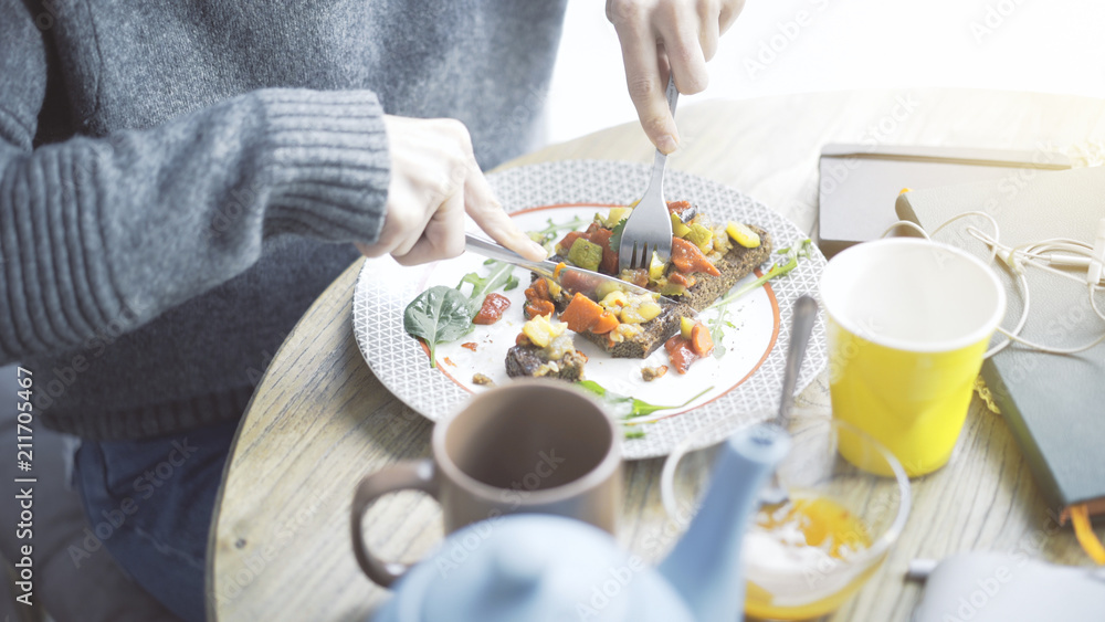A close up of female hands cutting a tartine of a stew salad on a bread lying on a plate A close up of female hands cutting a tartine of a stew salad on a bread lying on a plate