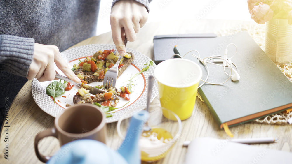 A close up of female hands cutting a tartine of a stew salad on a bread lying on a plate A close up of female hands cutting a tartine of a stew salad on a bread lying on a plate