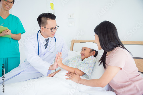 Young asian girl patient smiling and touching hand with doctor while lying on bed