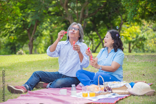 Happy asian retired couple blowing bubbles in park