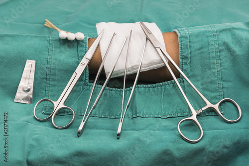 Suture set.clamp, mayo,blade, scissors,forceps,guaze,cotton butt with green cloth on patient. in the emergency room.