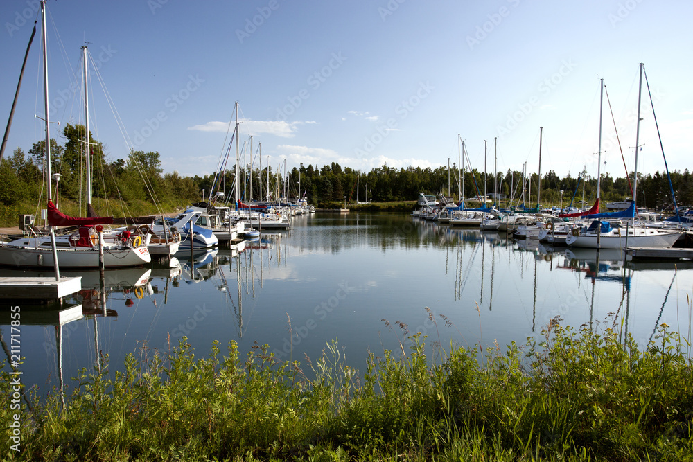View of a marina on Lake Superior full of boats and sailboats. Clear blue sky and calm water reflecting the scene.