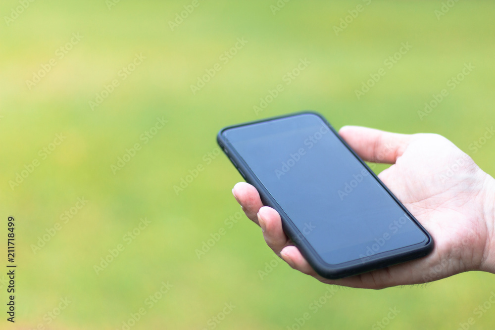 Close-up black smartphone on a man hands on green background with copy space .