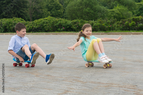 boy and girl ride in a park on a skateboard while sitting