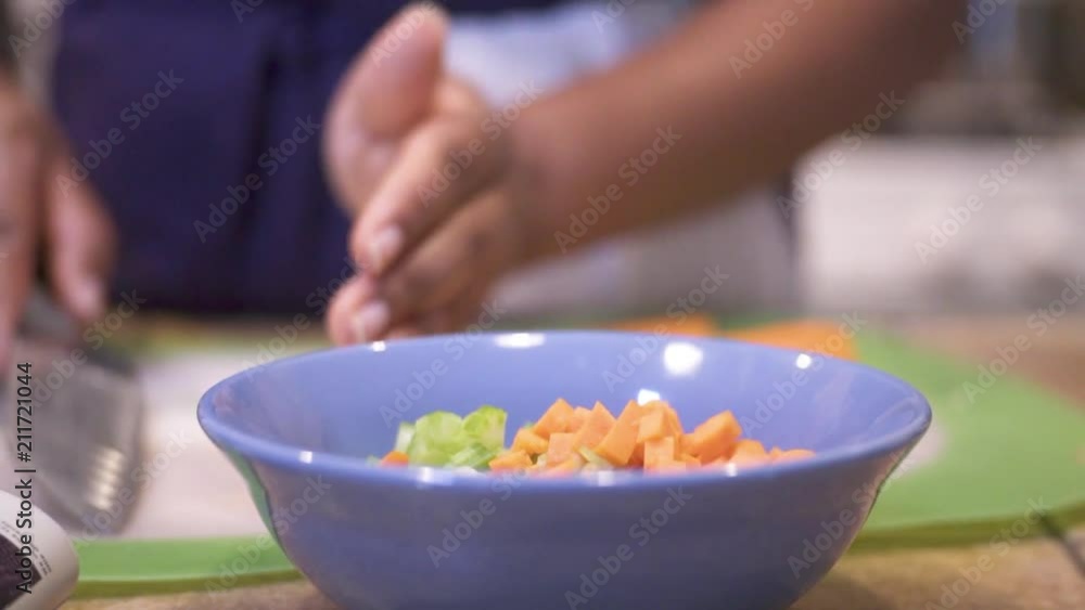 Closeup on hands – black woman scoops up diced carrots with knife and moves to blue bowl Closeup on hands – black woman scoops up diced carrots with knife and moves to blue bowl