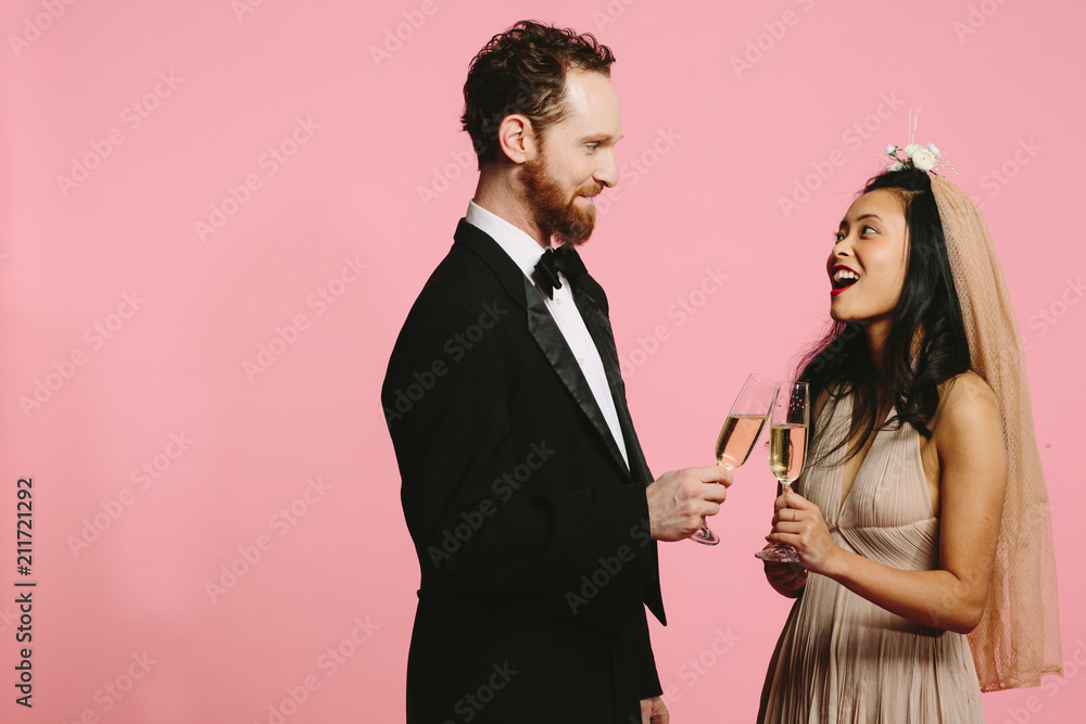 A smiling portrait of a bride and groom toasting with champagne glasses, isolated on pink