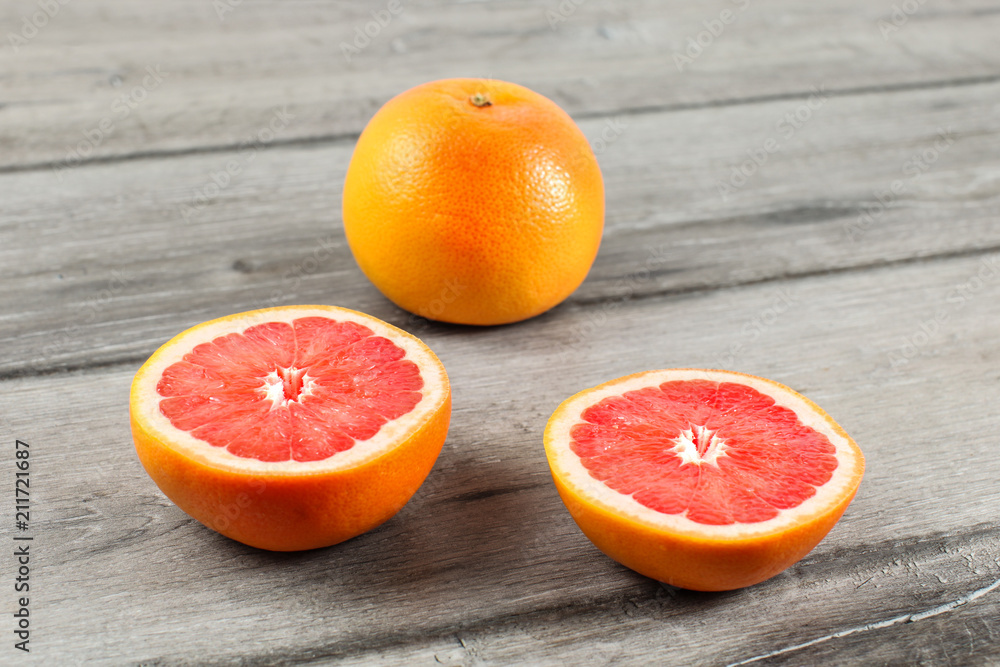 Pink grapefruit cut to half, with other whole citrus in background, placed on gray wood table. Pink grapefruit cut to half, with other whole citrus in background, placed on gray wood table.