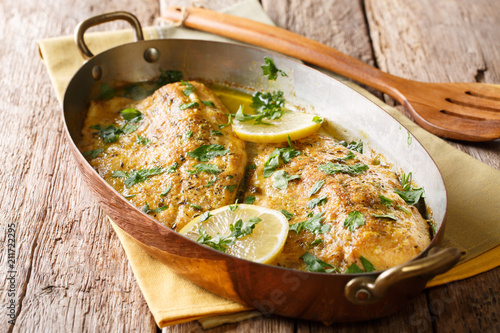 Served baked trout fillets with garlic butter sauce, lemon and parsley in a copper pan. Italian food. horizontal