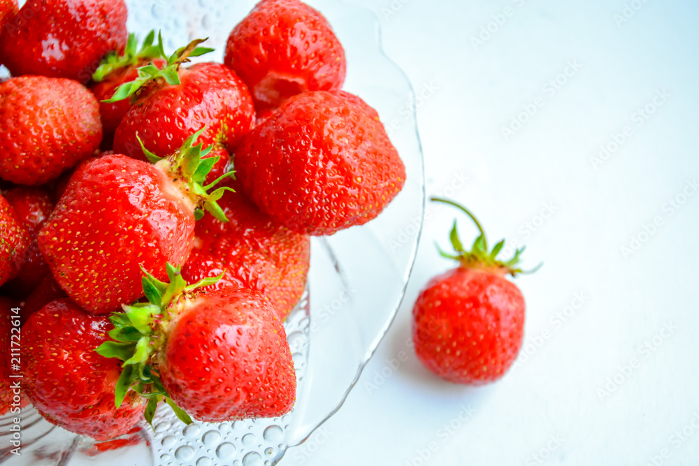 Red ripe strawberry with green leaves in a transparent glass plate on a light background Red ripe strawberry with green leaves in a transparent glass plate on a light background