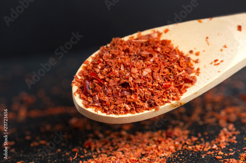 Spice red, ground, sharp bitter pepper is pouring out, a shovel is flying from a wooden scoop. Dark background