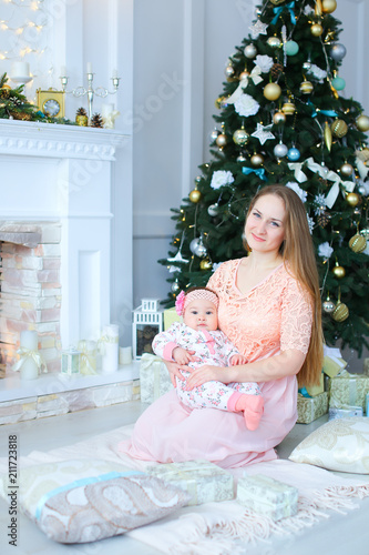 Happy caucasian woman gifting little daughter presetn near decorated fireplace. Concept of celebrating winter holidays and playing with baby. photo