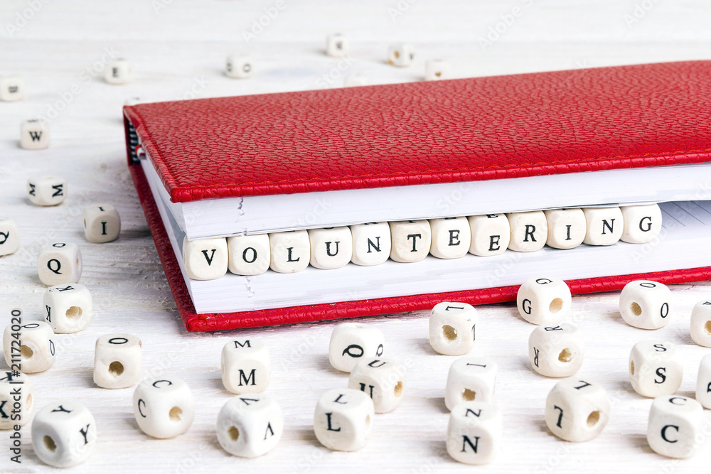 Word Volunteering written in wooden blocks in red notebook on white wooden table. Word Volunteering written in wooden blocks in red notebook on white wooden table.
