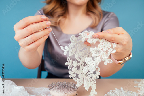 close-up hands of woman seamstress tailor ( dressmaker) designer wedding dress sews beads to lace on a blue background in the studio