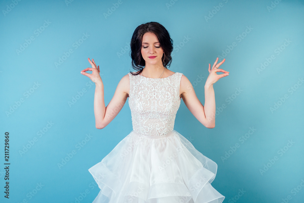 young and beautiful calm woman bride with makeup in chic white wedding dress practicing yoga and meditating in studio on a blue background . young and beautiful calm woman bride with makeup in chic white wedding dress practicing yoga and meditating in studio on a blue background .